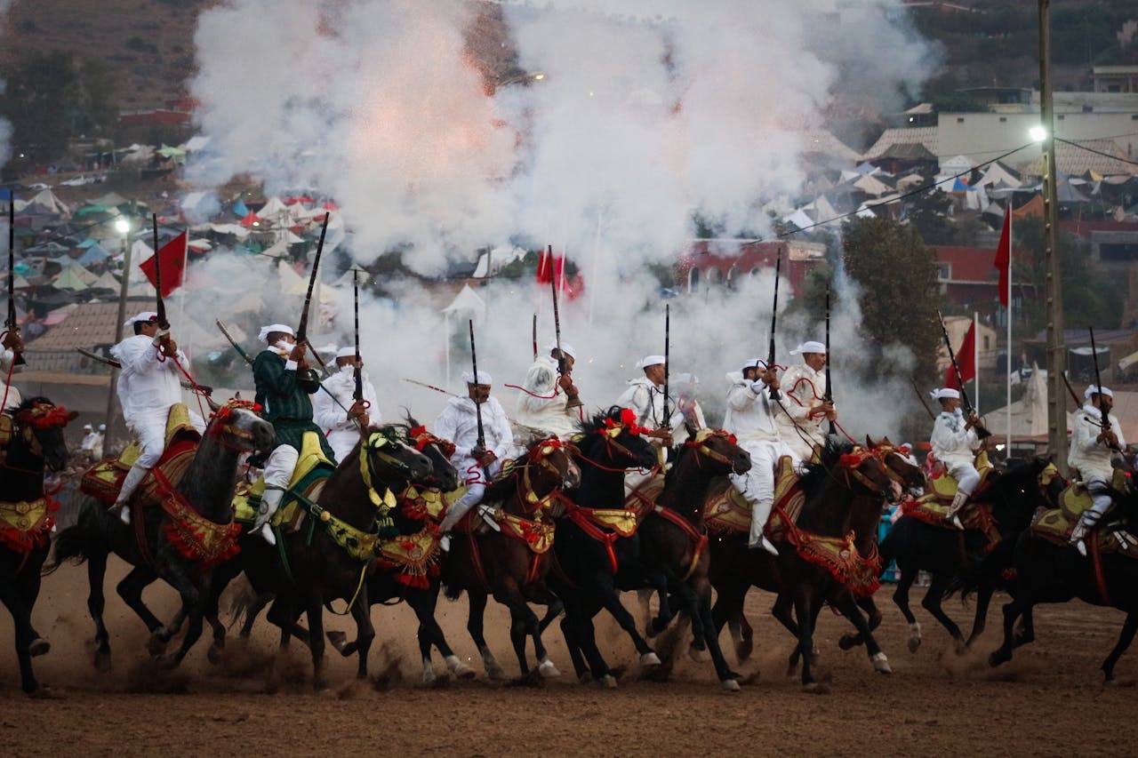 A dramatic display of Moroccan Tbourida with horsemen in traditional attire, gunsmoke, and vibrant energy.